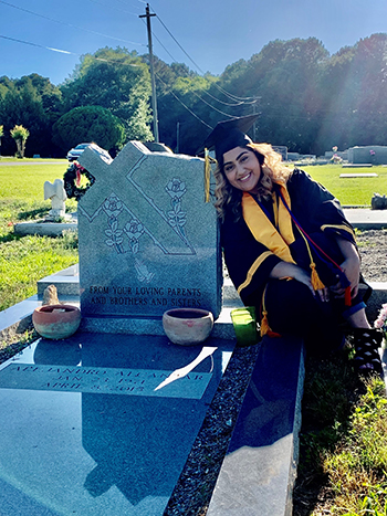 Photo of Isabel Alcantar smiling and wearing her graduation cap and gown at her father's gravesite. 