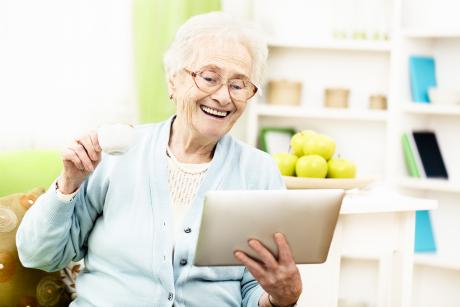 an older woman holding and looking at a tablet and laughing