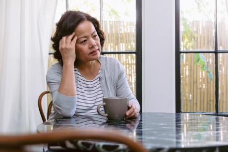 A woman sits at a table with a coffee cup looking upset