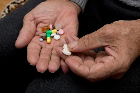 closeup of hands of older man holding pills
