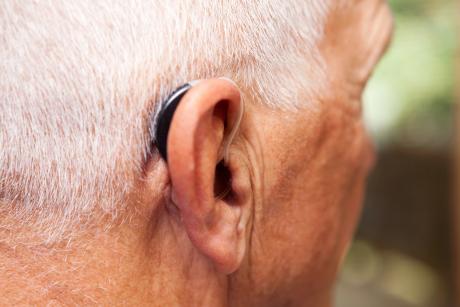 Older man's ear with with a very modern, low-profile and discrete hearing aid.
