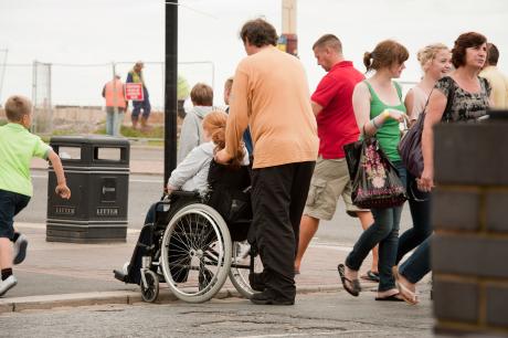 people negotiating curb at crowded crosswalk in wheelchair