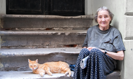 Photo of older woman accompanied by cat sitting on building front steps