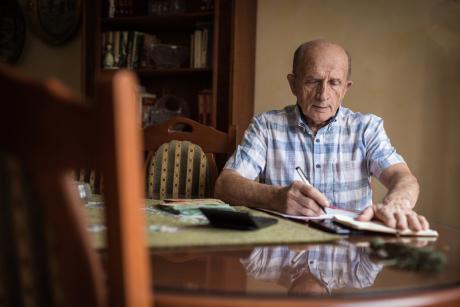 An older man sits at a table, doing paperwork.
