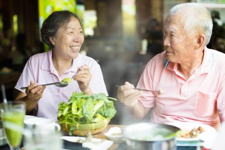 And older Asian couple smiles while having a meal together