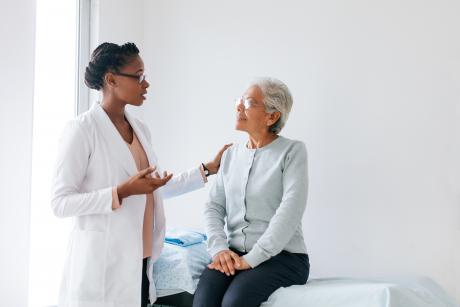 A doctor talks with an older patient. Both are Black women.