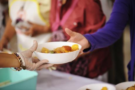 Older woman reaching for bowl of food from volunteer