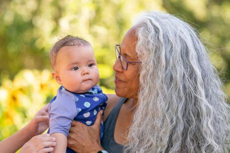 Older Indigenous woman with long gray hair holds baby