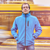 An older man in a blue jacket looking sad, a bus whizzing by behind him