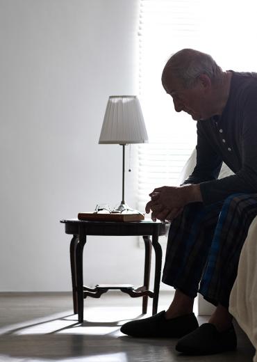 Older man sitting on bed looking serious