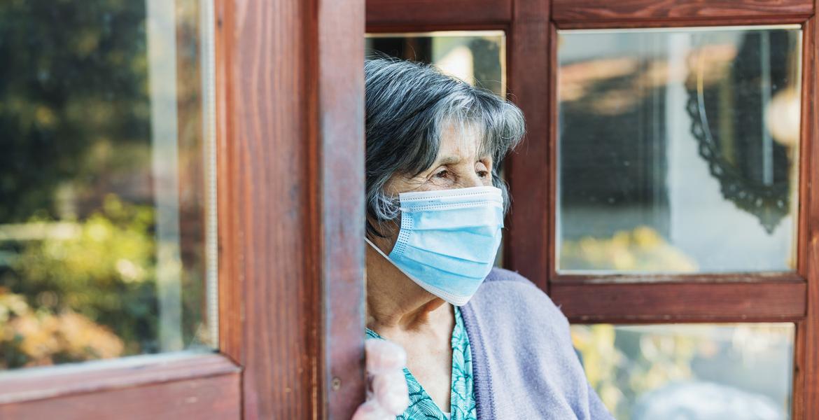 an older woman stands in a doorway looking outside, she's wearing a mask