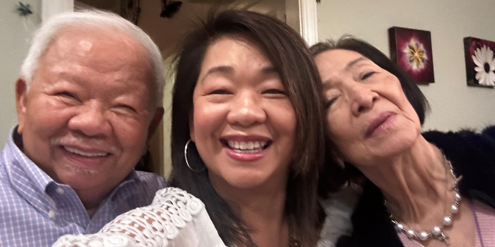 Grace Schauf smiles in a selfie with her two older parents indoors.