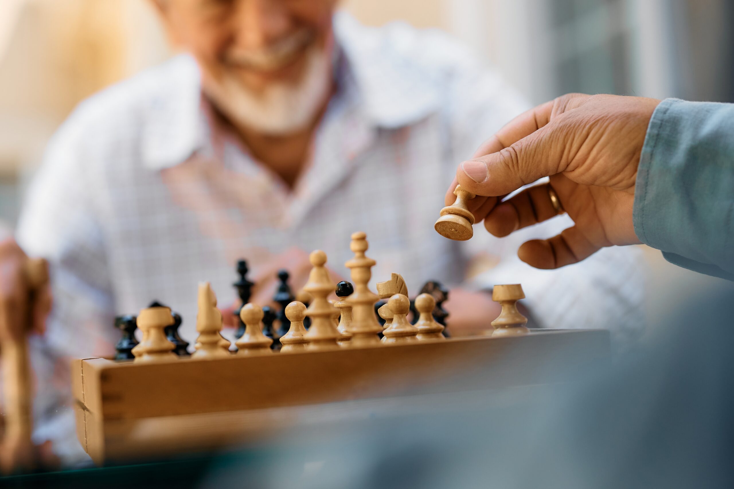 Close,Up,Of,Seniors,Playing,Chess,On,Patio,In,Nursing